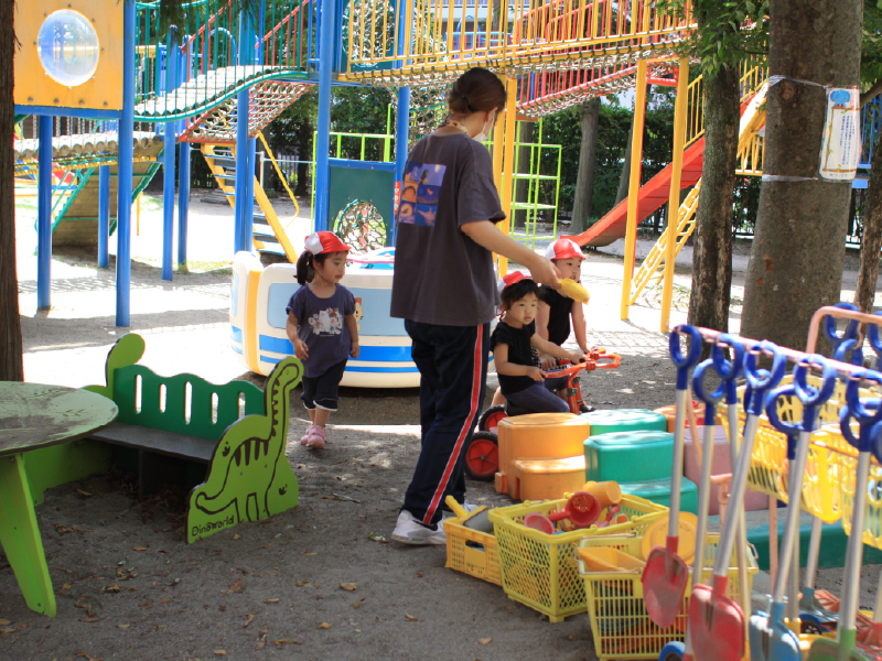 園庭で先生と一緒に遊ぶ満3歳児クラスの子どもたち。